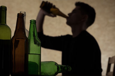Beer bottles in the foreground, shadowed teenage male in the background drinking