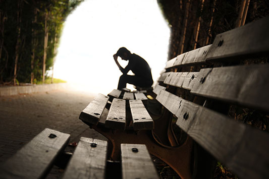 Lonely man sitting on a bench in a dark tunnel