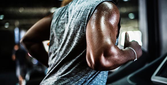 Black man running on a treadmill. We see his torso, focusing on his arms and shoulder as the sweat beads and drips off him.