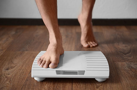 A man's feet stepping onto a bathroom scale